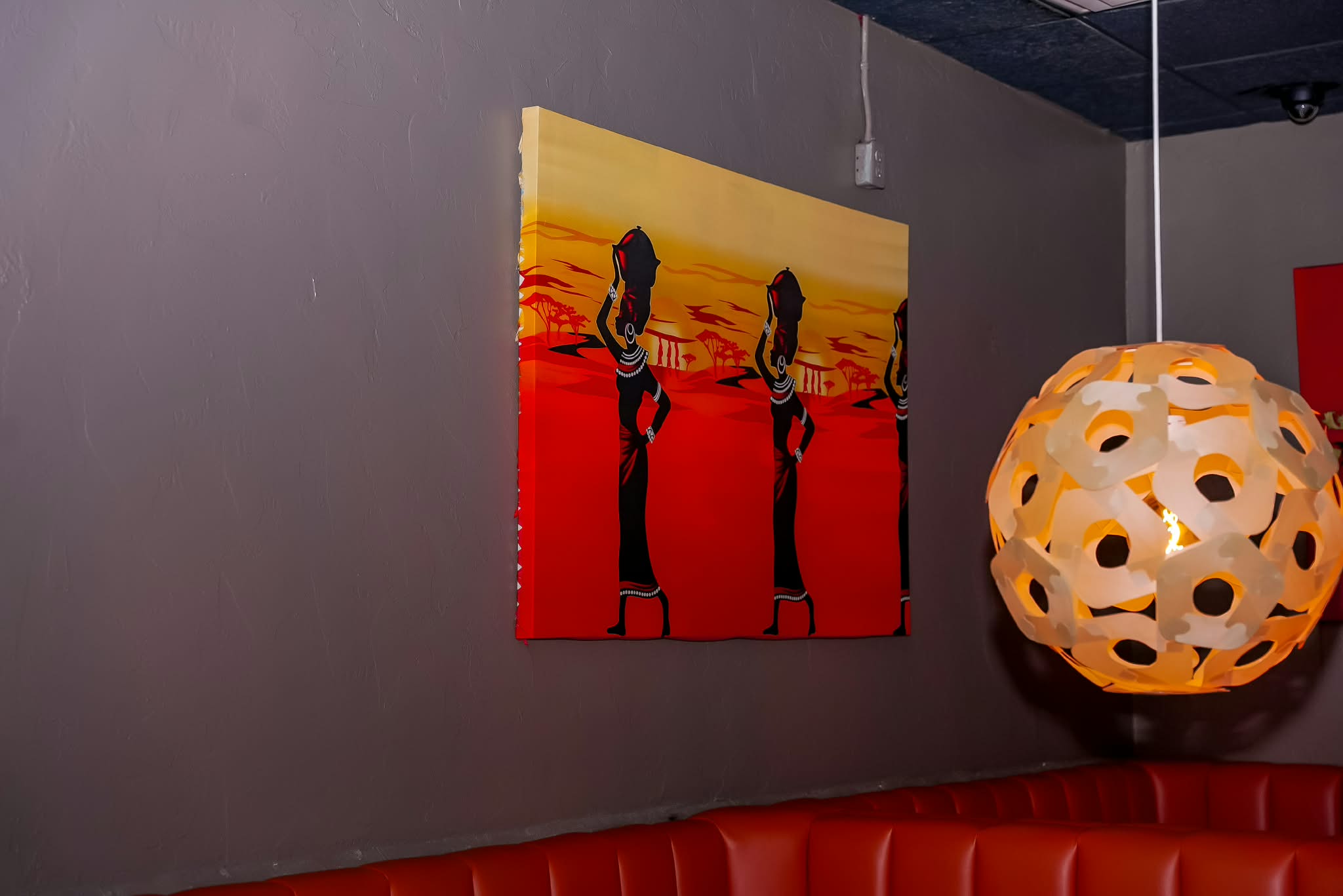 Hand-painted canvas art and a woven pendant lamp above the orange banquette seating
